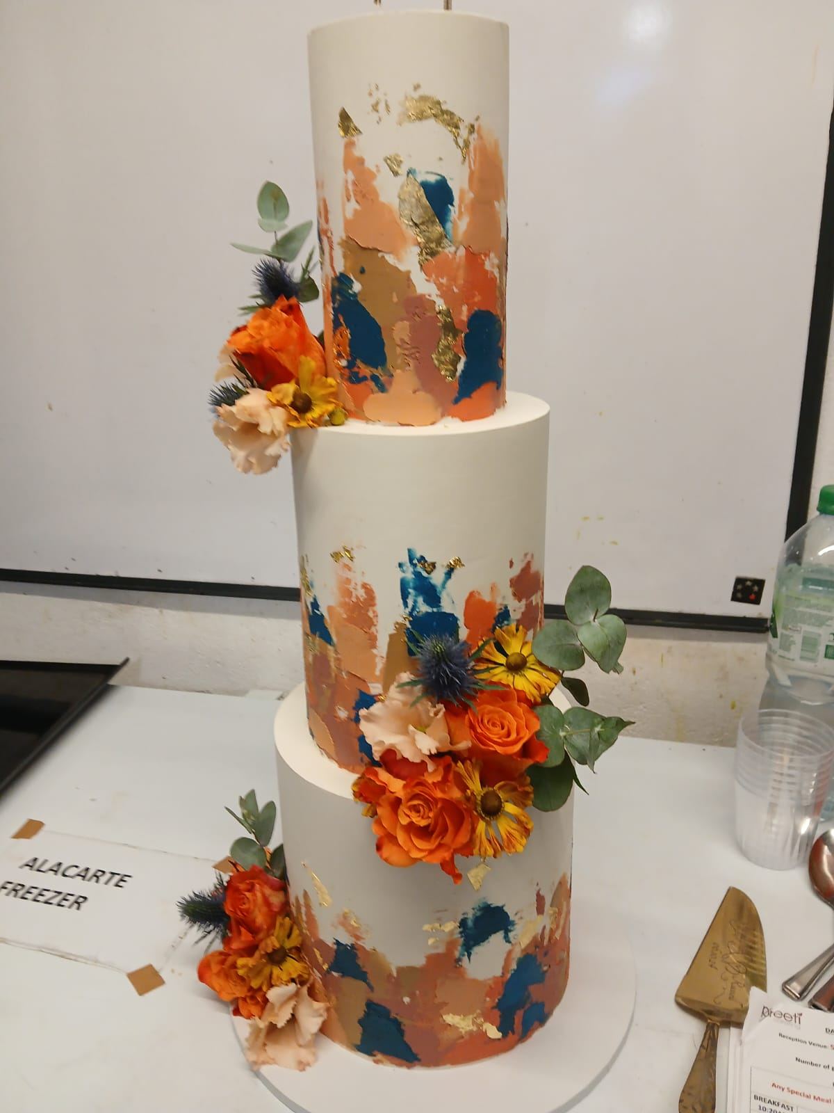 Three-tier wedding cake with fresh flowers and gold leaf